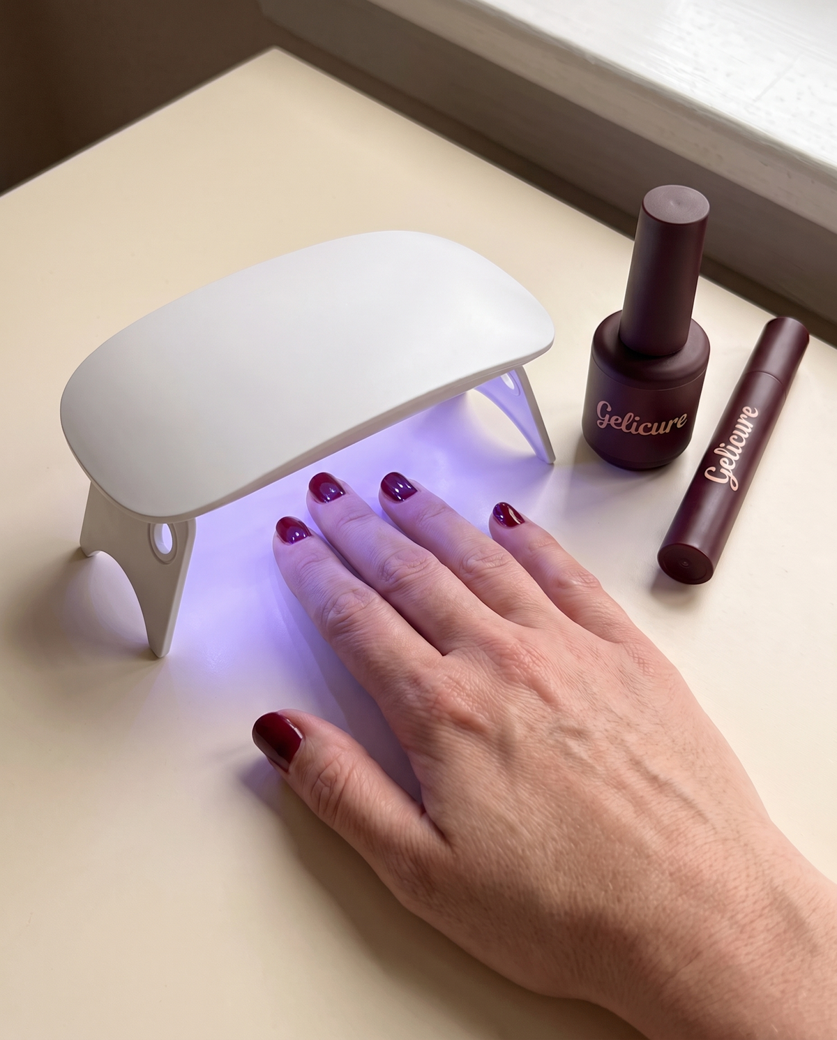 Hand under the Gelicure UV lamp with top coat and pen